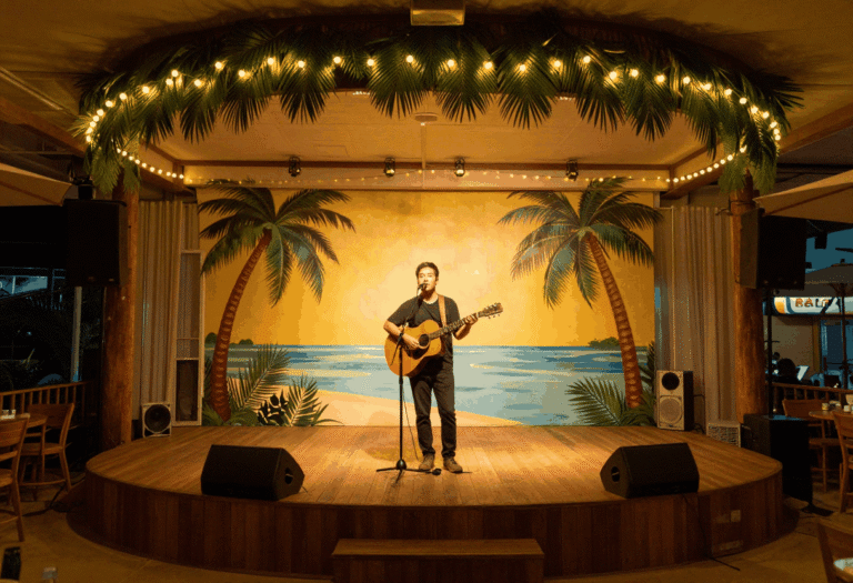 Illustrative AI-generated image of a small theater stage decorated with tropical string lights and palm decor