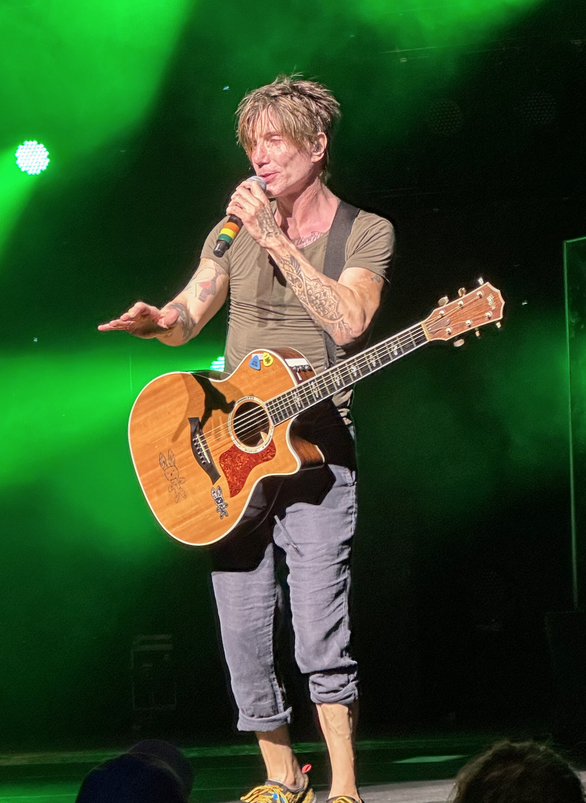 John Rzeznik of the Goo Goo Dolls performing live on stage with an acoustic guitar under green stage lighting — photo from a 2023 show in Syracuse, New York, not the Tampa date.