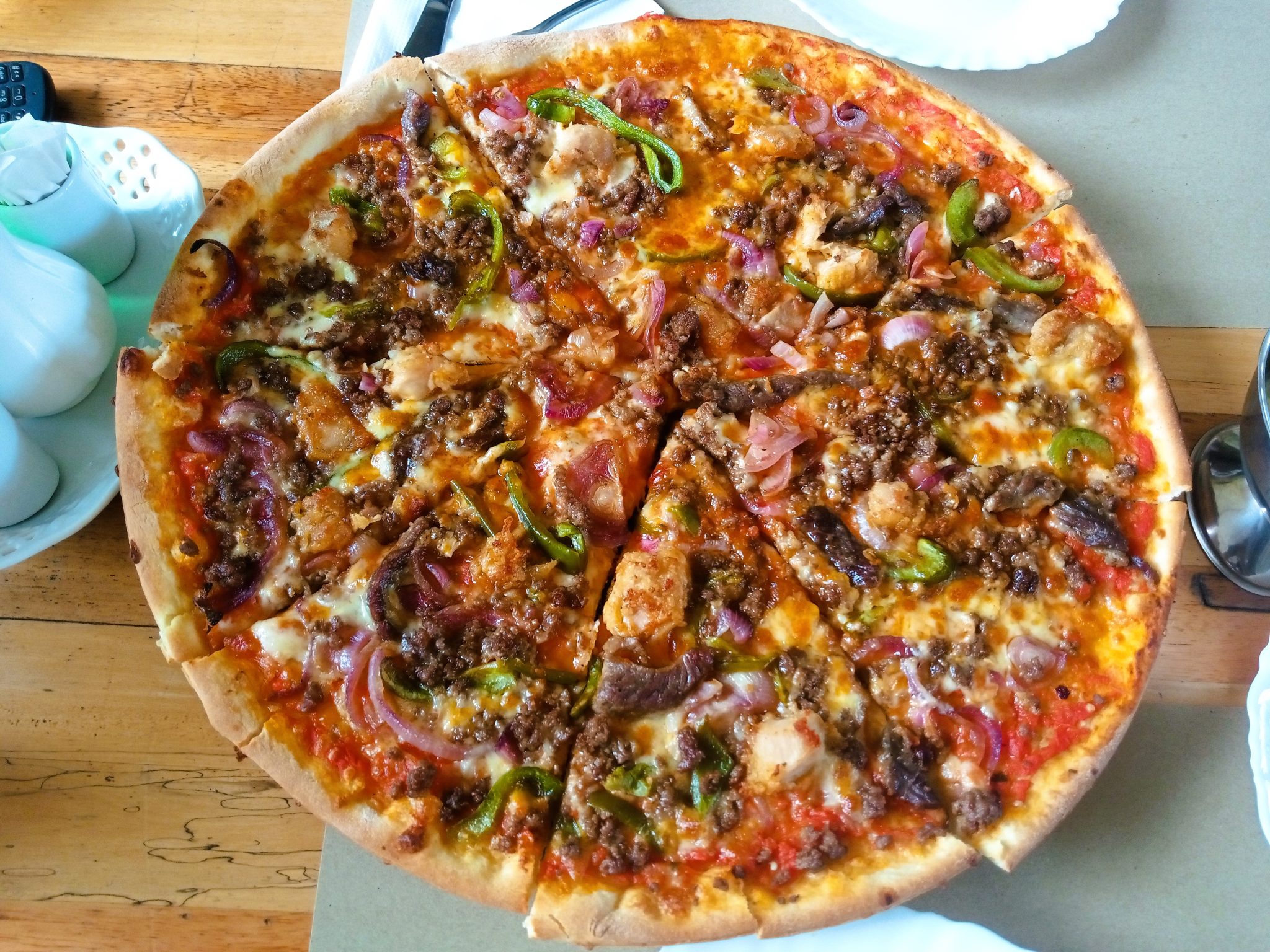 Overhead view of a large supreme pizza with sausage, peppers and red onion on a wooden table