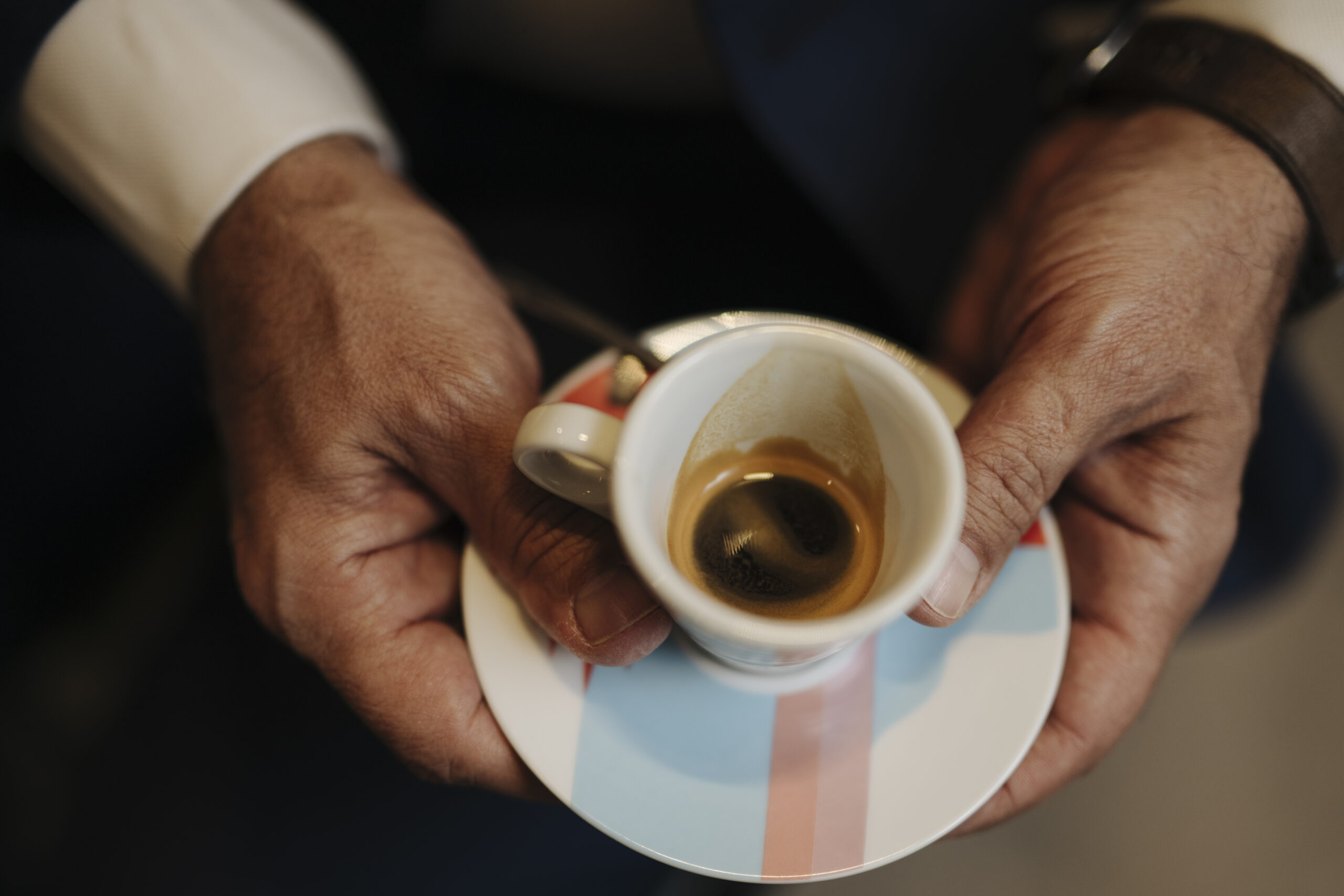 Close-up of a pair of hands holding a small cup of espresso on a saucer