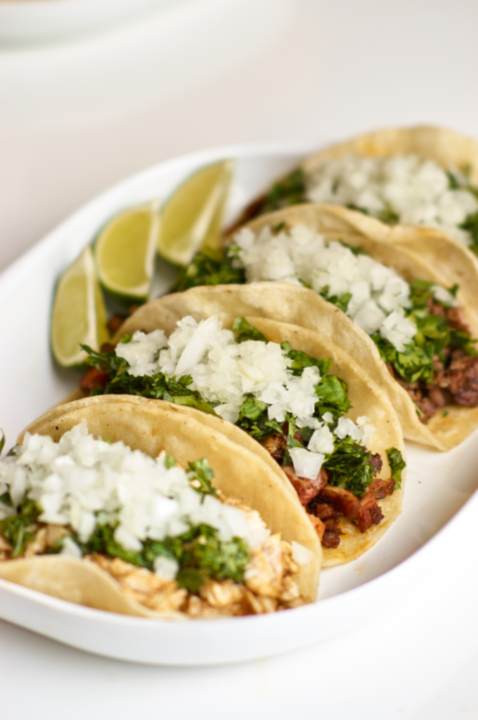 Four corn-tortilla street tacos topped with cilantro and diced onion, served with lime wedges
