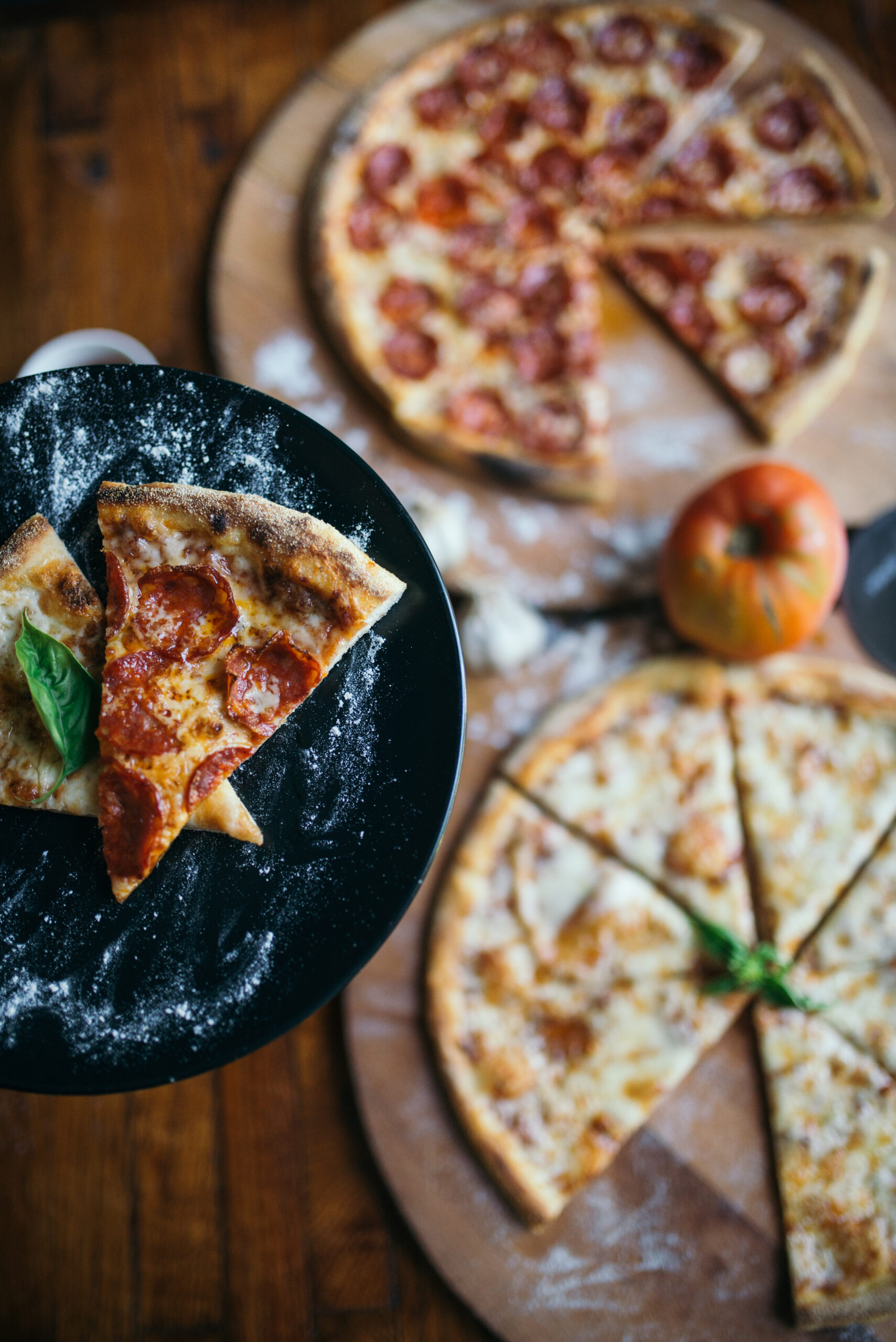 Pepperoni and cheese pizzas on wooden boards with a slice lifted onto a dark serving plate